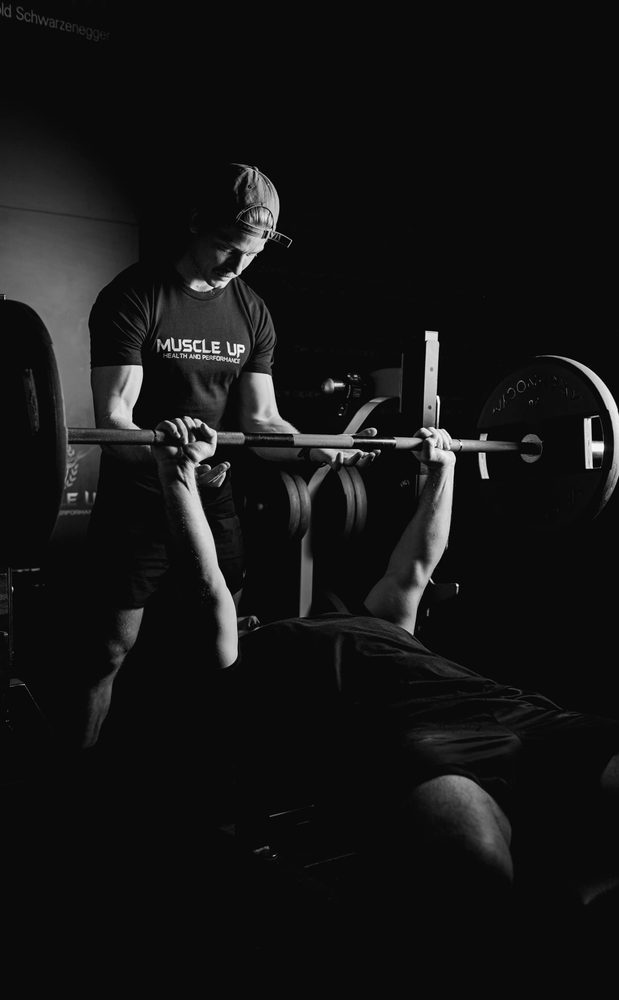 A member in a cap and Muscle Up tee setting up a barbell bench press